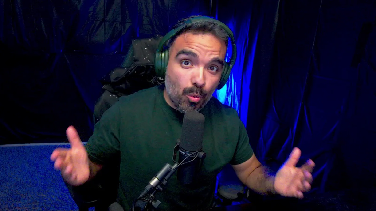 Aniimo creator AniimoSync talking to camera in a green headset and T-shirt in front of a blue-lit curtain, at the end of the Irisalis video